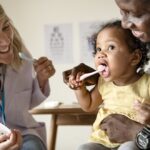 dentist promoting children's dental health by teaching child how to brush teeth in dental chair at dentist