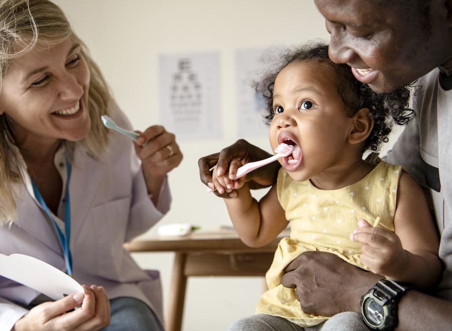 dentist promoting children's dental health by teaching child how to brush teeth in dental chair at dentist